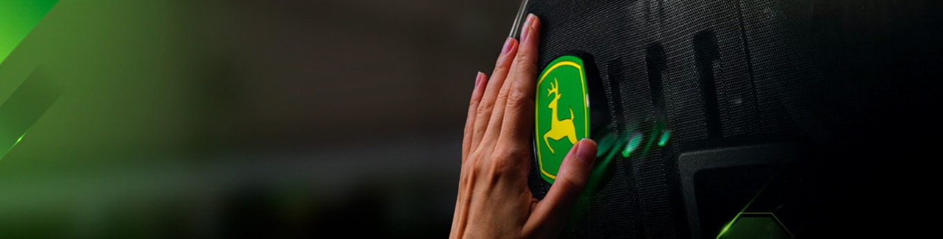 Fondo verde, en el centro una mano de piel clara toca el símbolo de John Deere.