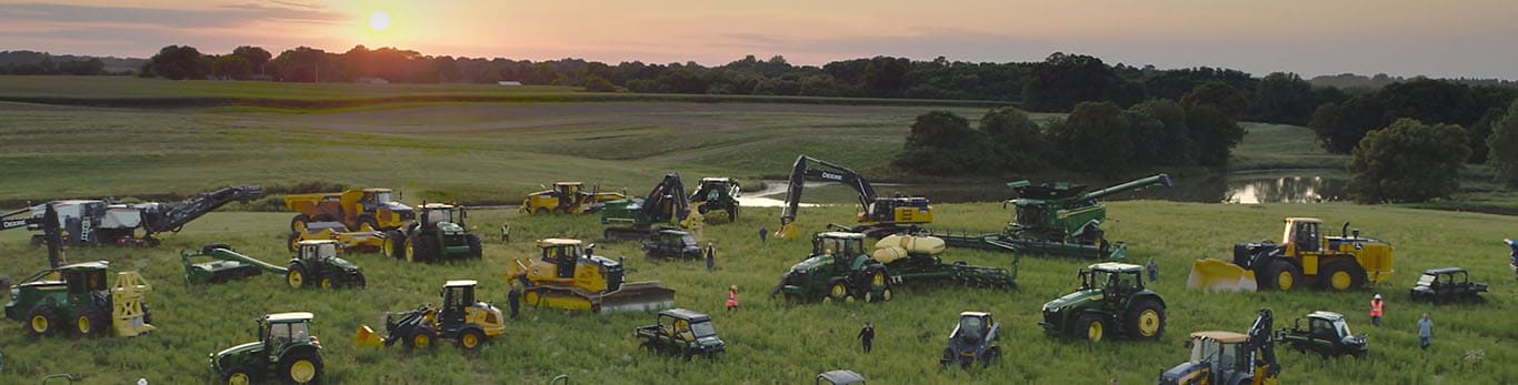 Personas caminando entre distintos equipos de John Deere en un gran campo.