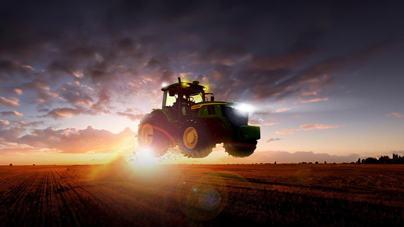 Una máquina John Deere volando sobre el campo al atardecer.
