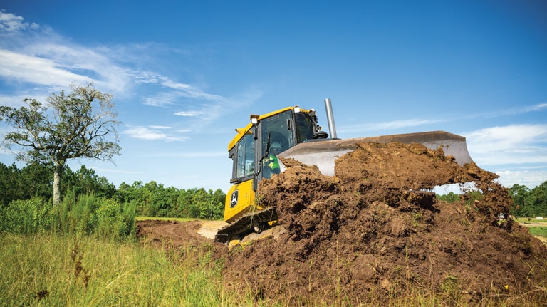 Vista frontal de un bulldozer 450P empujando tierra con árboles en el fondo.