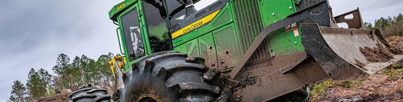 A John Deere 640L-II Log Skidder drives through a muddy landing in the forest