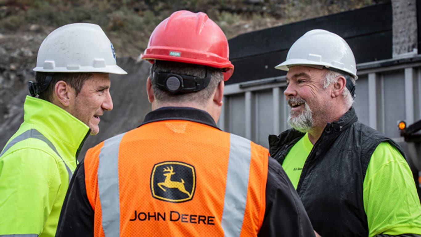 Dos hombres hablan entre sí con un chaleco de seguridad y un casco de protección con el logotipo de John Deere.