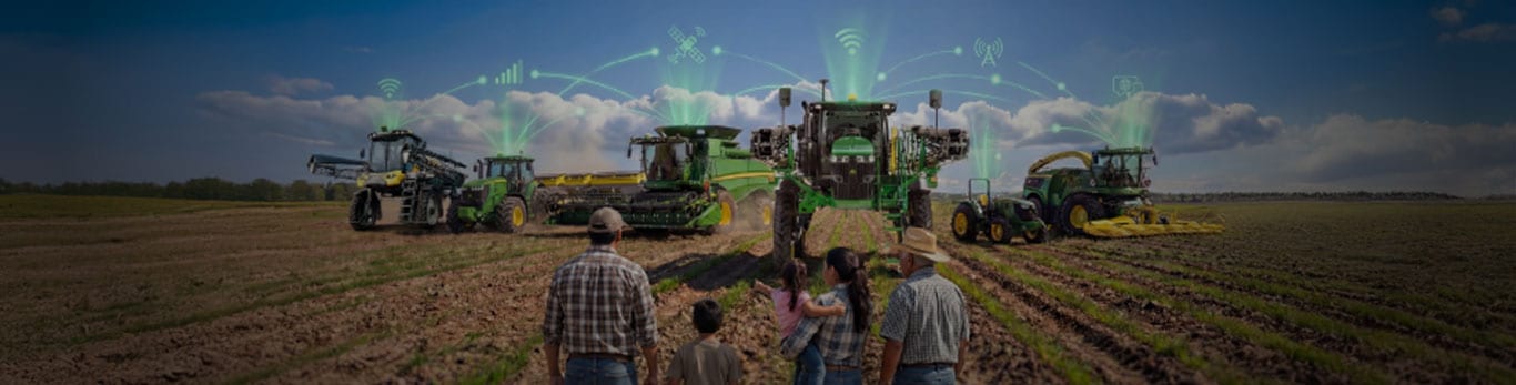 En el primer plano, una familia mirando el horizonte, en el fondo hay maquinaria John&nbsp;Deere en el campo, con s&iacute;mbolos de conectividad entre las m&aacute;quinas