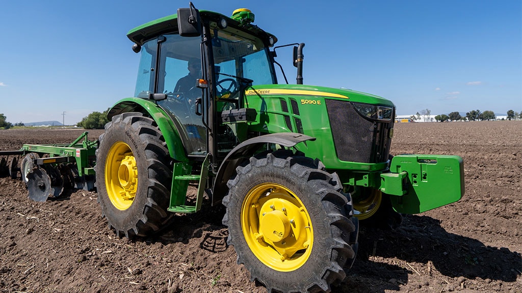 Tractor John Deere de alta potencia sobre un terreno rural, en perspectiva frontal.