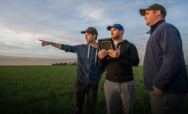 Banner web que muestra a 3 hombres en el campo, uno de ellos señalando a lo lejos y otro utilizando una tablet con la aplicación Operations Center™ que mantiene al ecosistema conectado.