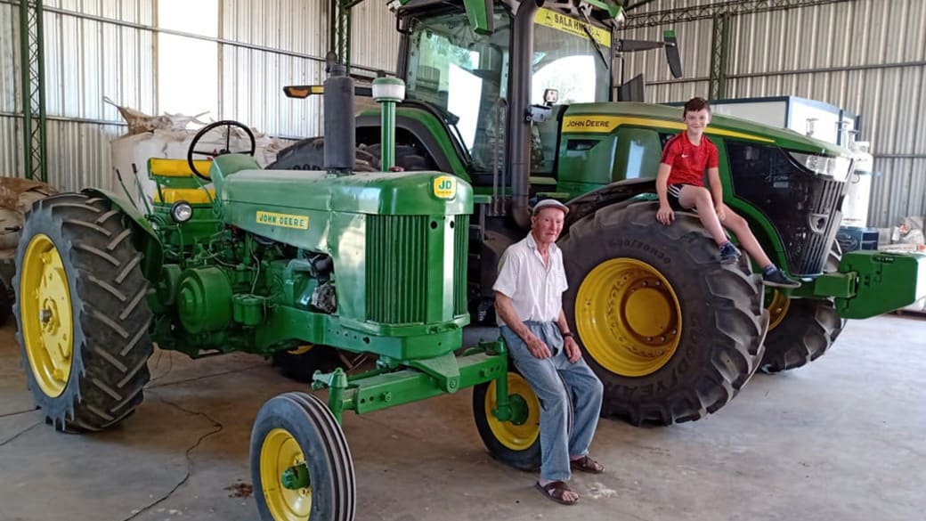 Imagen de abuelo y nieto, con el primer tractor de la familia y su reciente adquisición, un 7R 230