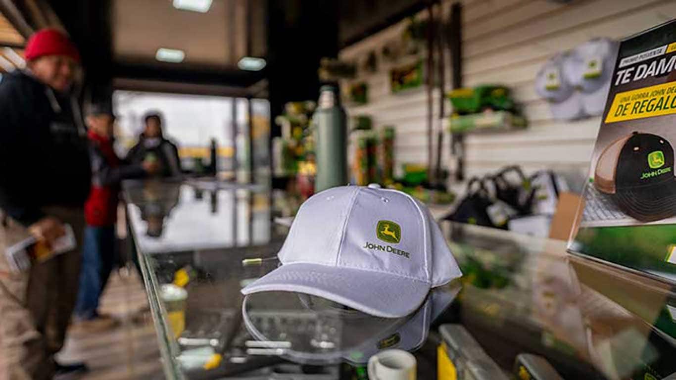 Boné branco John&nbsp;Deere no balcão de uma loja de distribuição e nas imagens de fundo dos clientes