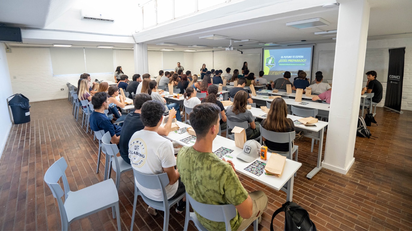 Vista de un aula, con alumnos sentados en escritorios observando una pantalla de desafío