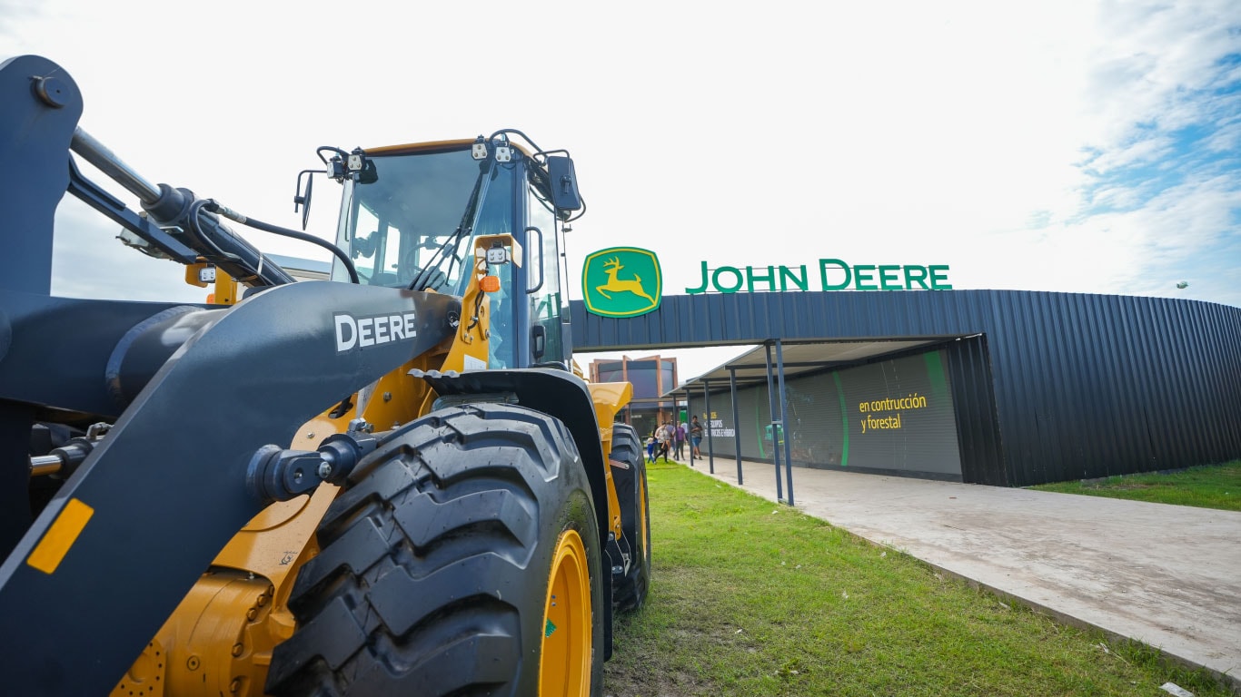 Una máquina de construcción John Deere frente a un panel con el logo de la empresa.