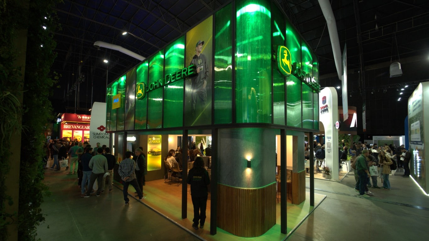 Stand de John Deere iluminado en verde durante una exposición agroindustrial, con visitantes recorriendo el espacio.