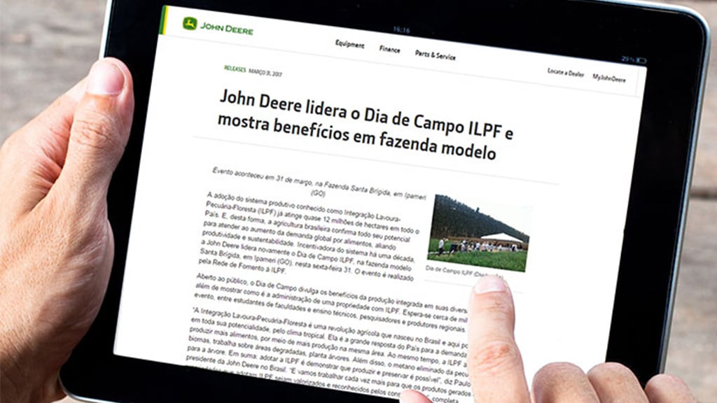 Artigo da John Deere exibido em um tablet segurado em duas mãos