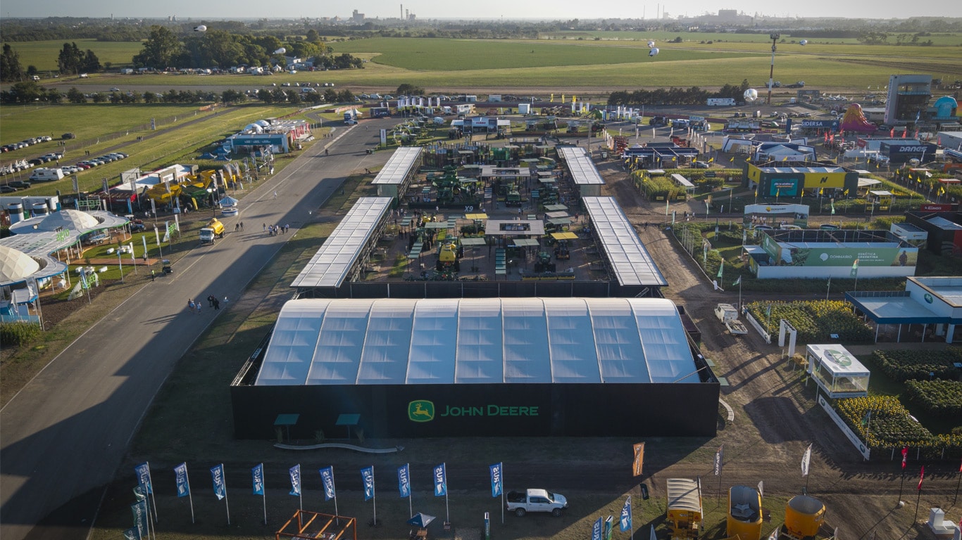 Vista a&eacute;rea del stand John Deere en Expoagro con equipos agr&iacute;colas al amanecer