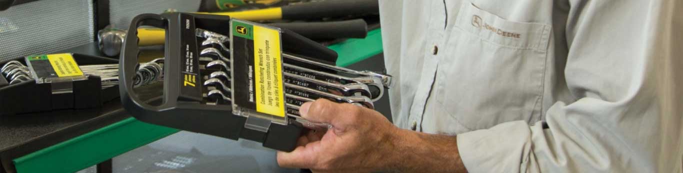 Un hombre sosteniendo un conjunto de herramientas John Deere dentro de una tienda, solo vemos sus manos.