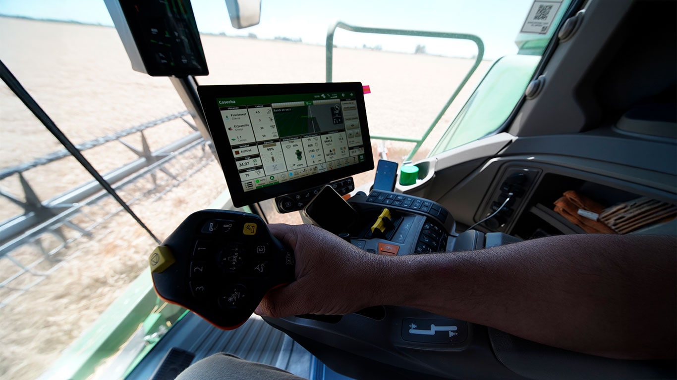Mano operando la cosechadora S7 dentro de la cabina, con un monitor al fondo.