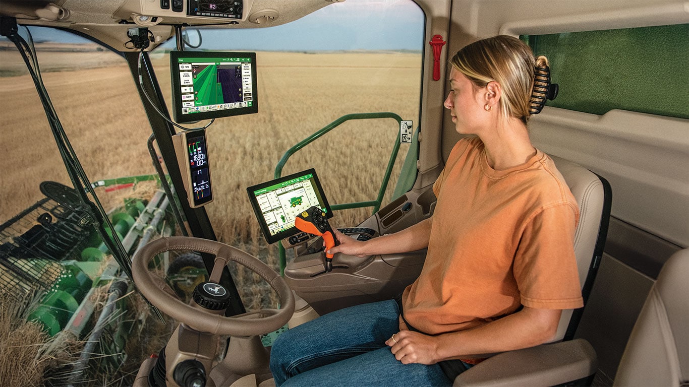 Una mujer rubia operando una cosechadora John Deere en la cabina.