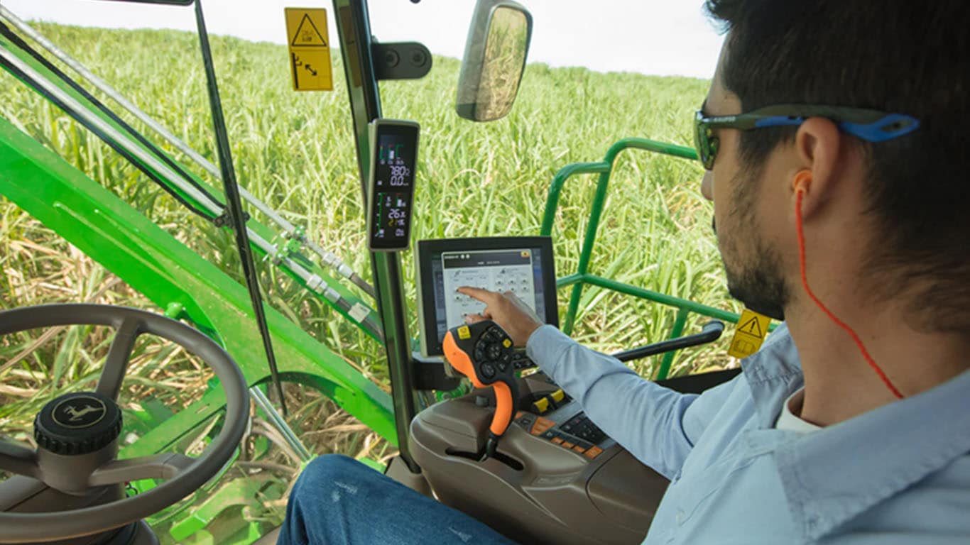 Un hombre trabajando dentro de una máquina John Deere, con un monitor
