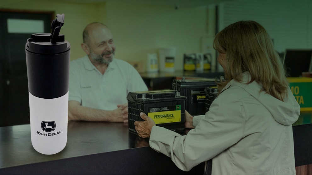 La imagen muestra a una mujer mayor comprando una batería que dice "Performance", mientras que al otro lado del mostrador hay un hombre mayor que la atiende. La imagen tiene un verde libre en la esquina superior derecha. En primer plano, en el lado izquierdo de la imagen, hay una botella en blanco y